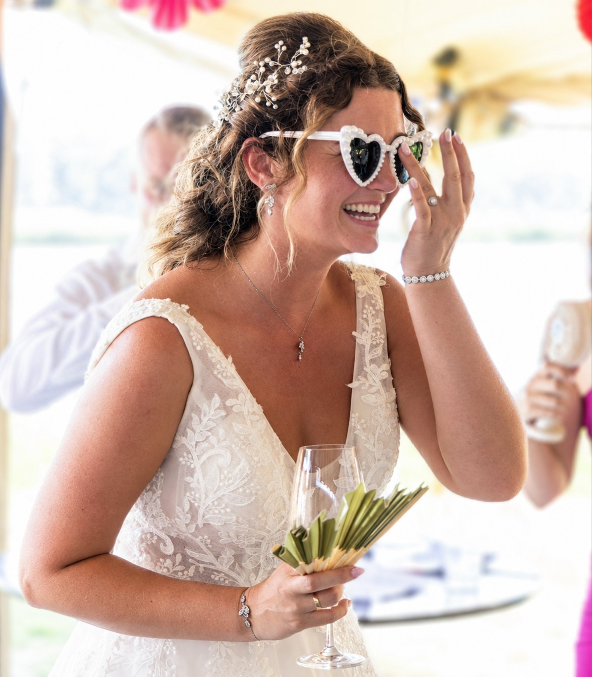 Bruid in een witte trouwjurk met geborduurde bloemen, lachend met een wijnglas in haar hand tijdens het bruiloftsfeest