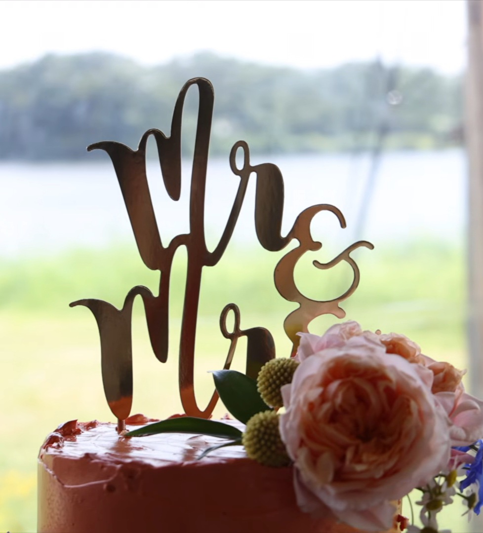 Bruidstaart met roze bloemen en een gouden Mr en Mrs taarttopper